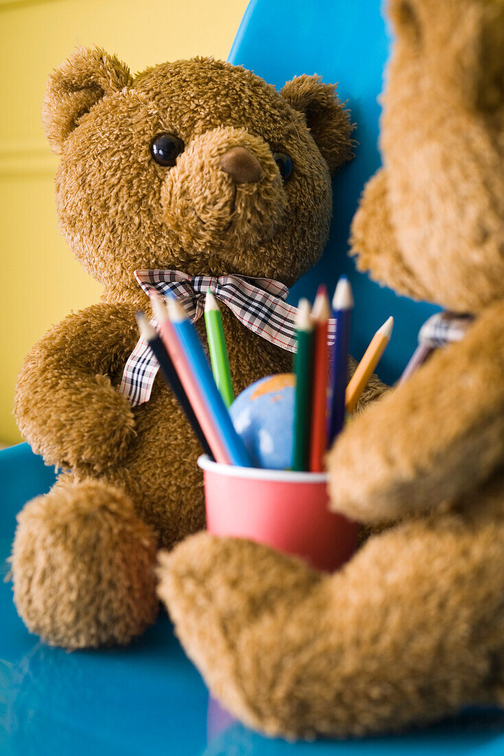 Teddy bears seated face to face with cup of colored pencils between them