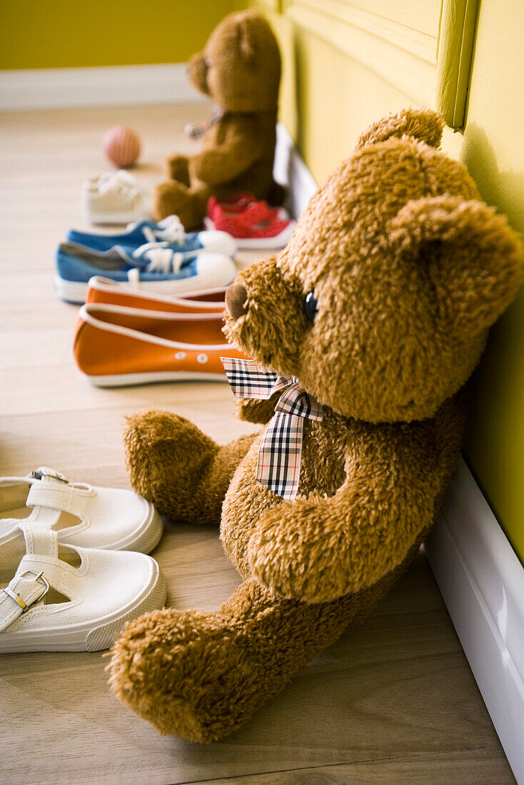 Teddy bears sitting on floor with several pairs of child's shoes
