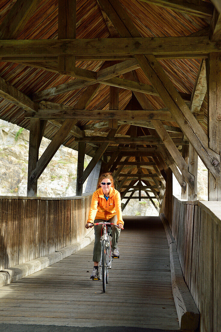 Fahrradfahrerin fährt über überdachte Holzbrücke, Urgen, Fließ, Tirol, Österreich