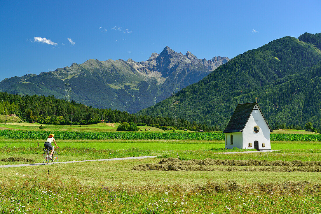 Fahrradfahrerin fährt Inn-Radweg entlang, Michaelskapelle und Ötztaler Alpen im Hintergrund, Karrer Höhe, Karres, Tirol, Österreich