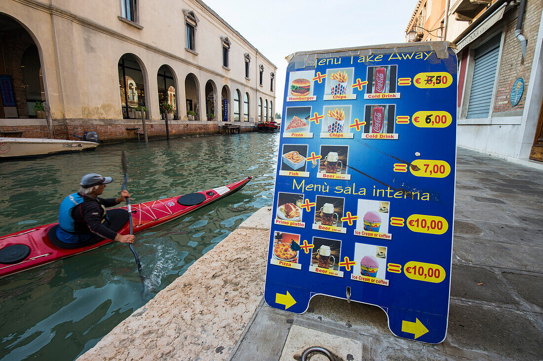 Man paddling past a fast food menu, Murano, Venice, Italy