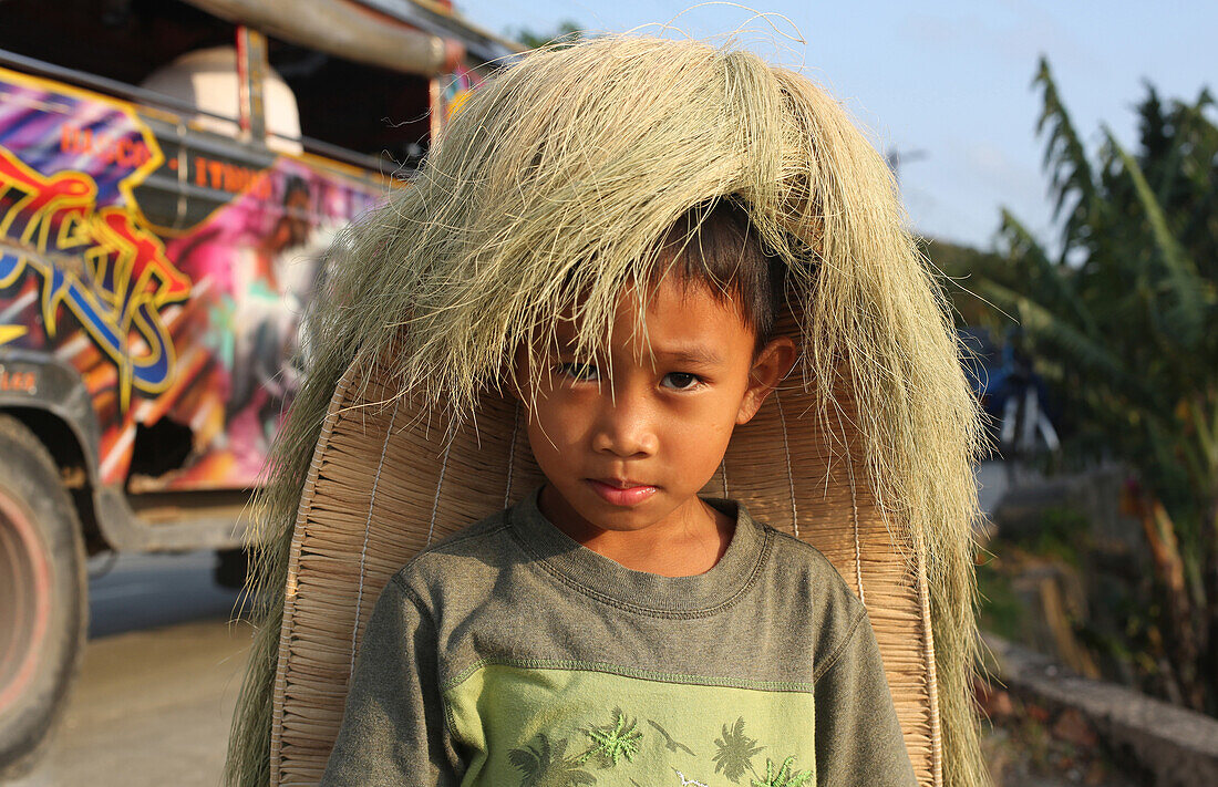 Boy wearing traditional straw wig with a jeepney in the background, Batan Island, Batanes, Philippines, Asia