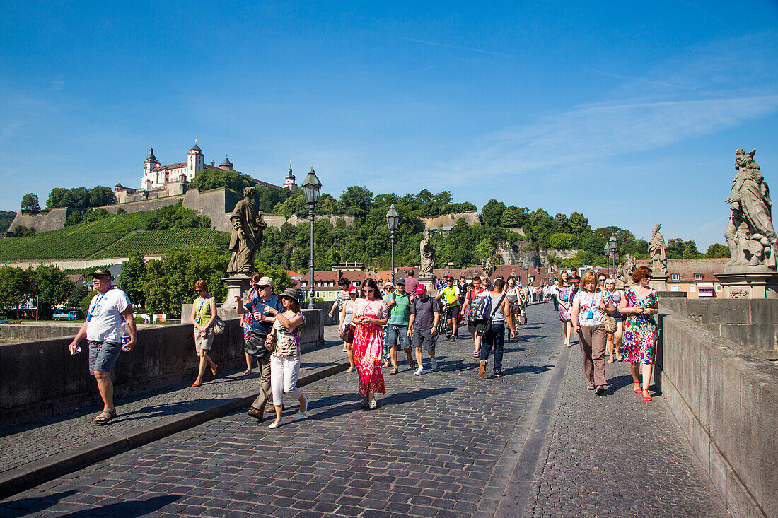 Touristen laufen auf Alte Mainbrücke über Fluss Main mit Festung Marienberg im Hintergrund, Würzburg, Franken, Bayern, Deutschland