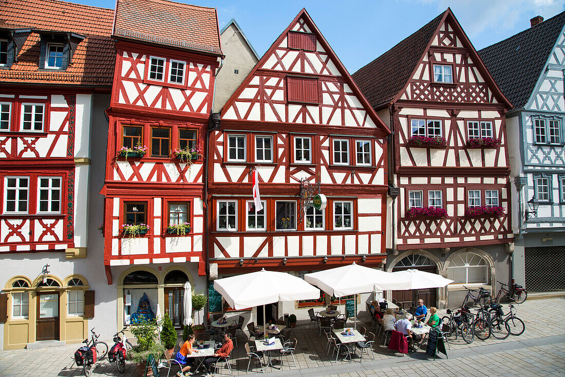 Menschen sitzen draußen vor Cafes und Restaurants der prächtigen Fachwerkhäuser in der Altstadt, Ochsenfurt, Franken, Bayern, Deutschland