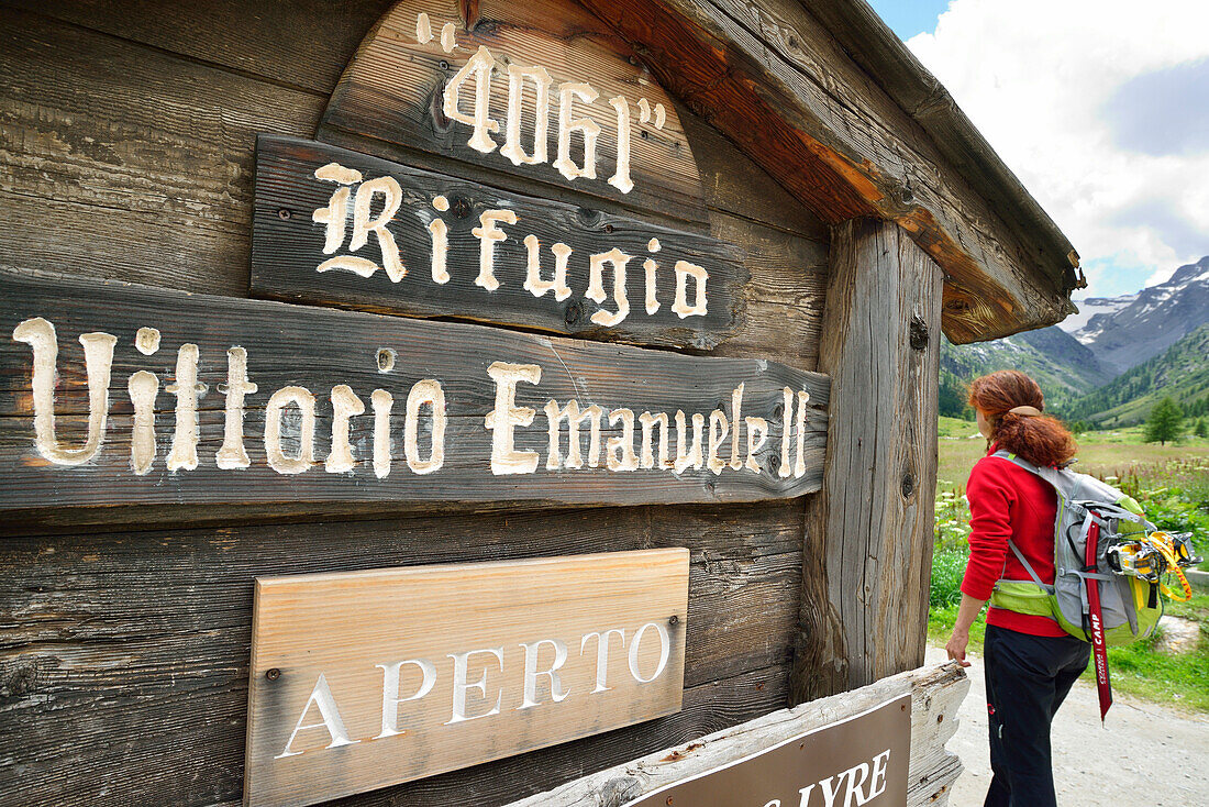Frau wandert an großem Schild des Rifugio Vittorio Emanuele II vorbei, Gran Paradiso, Nationalpark Gran Paradiso, Grajische Alpen, Aostatal, Aosta, Italien