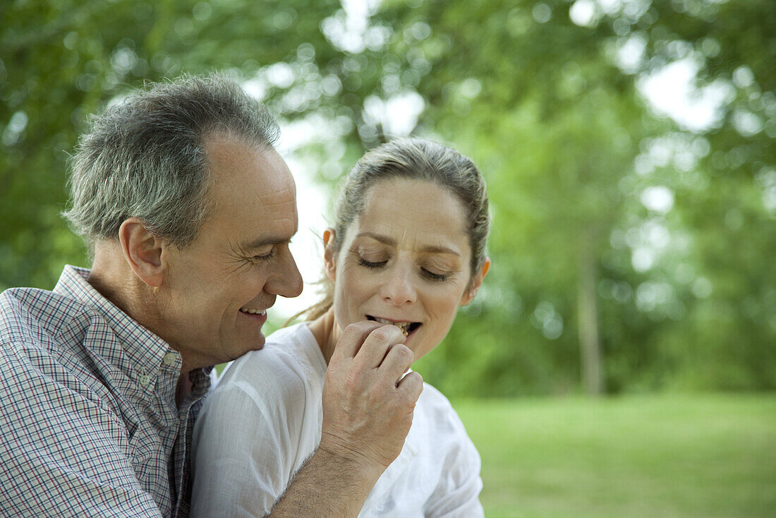 Mature couple together in park, man feeding woman