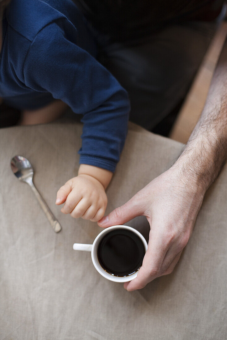 Man having cup of coffee while holding toddler son, cropped