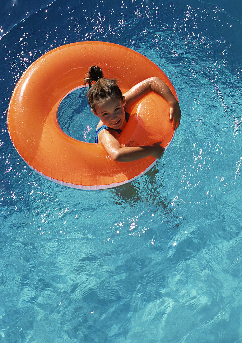 Young girl floating in inner tube in pool, shot from above.