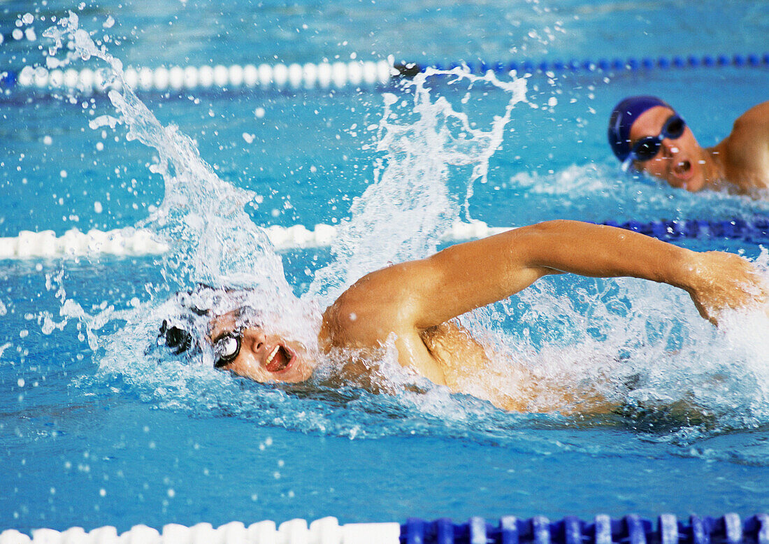 Male swimmers swimming freestyle in pool, close-up