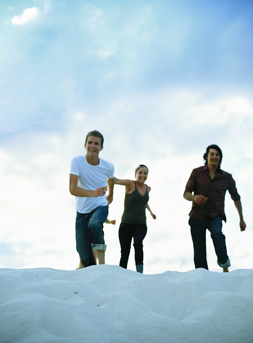 Two men and woman running on sand