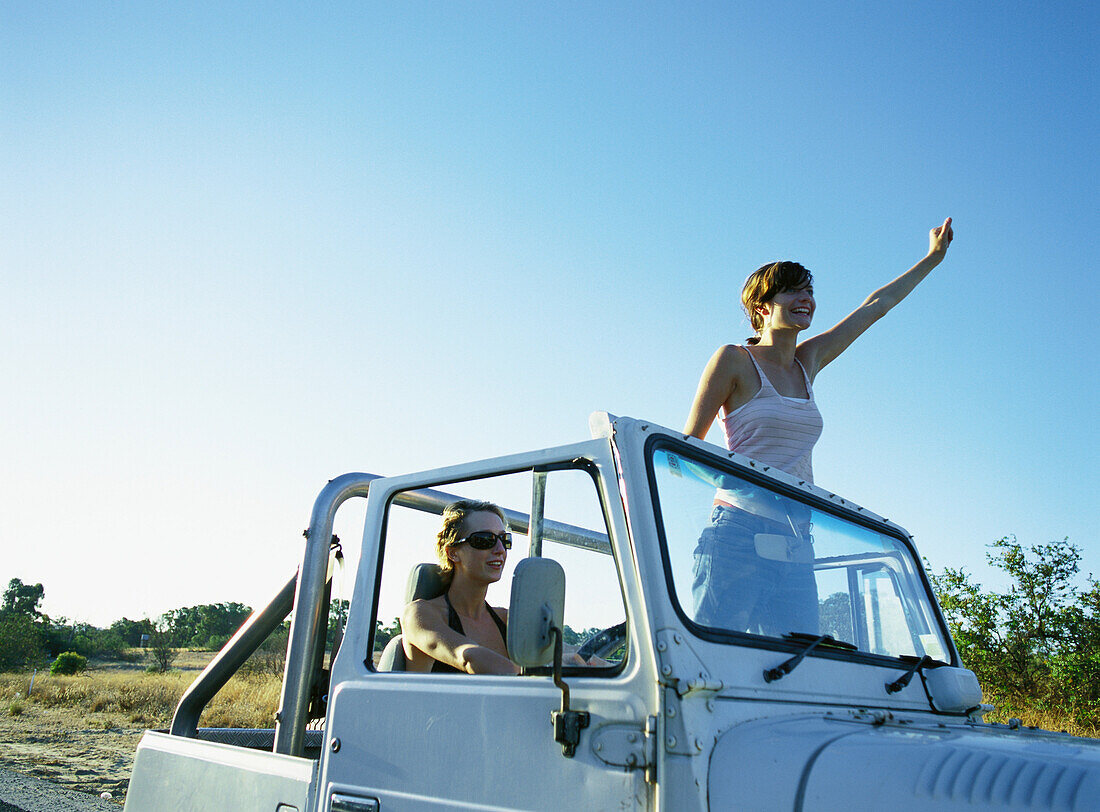 Two women in 4x4 vehicle, one standing up, waving