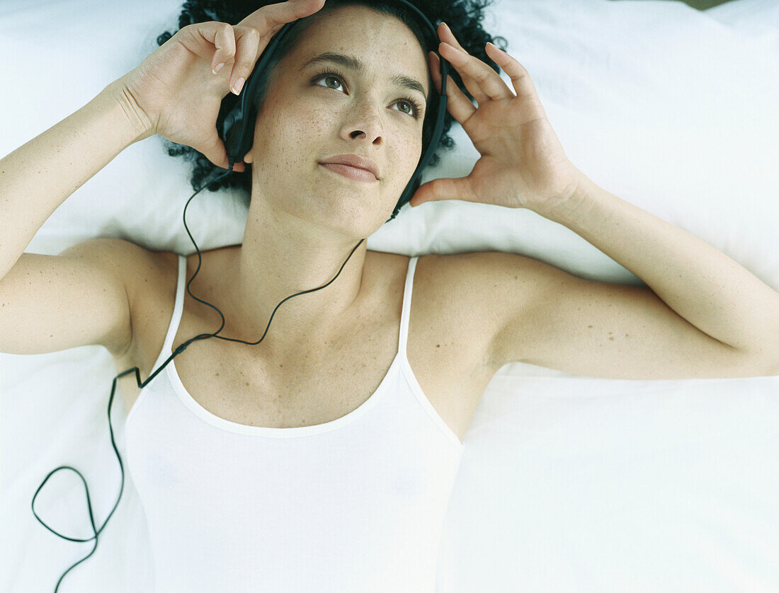 Frau auf dem Rücken liegend auf dem Bett mit Kopfhörern und Händen an der Seite des Kopfes