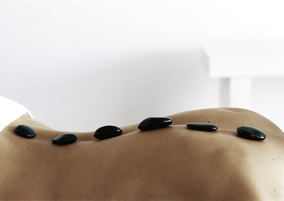Rücken einer Frau mit schwarzen Steinen entlang der Wirbelsäule, Nahaufnahme