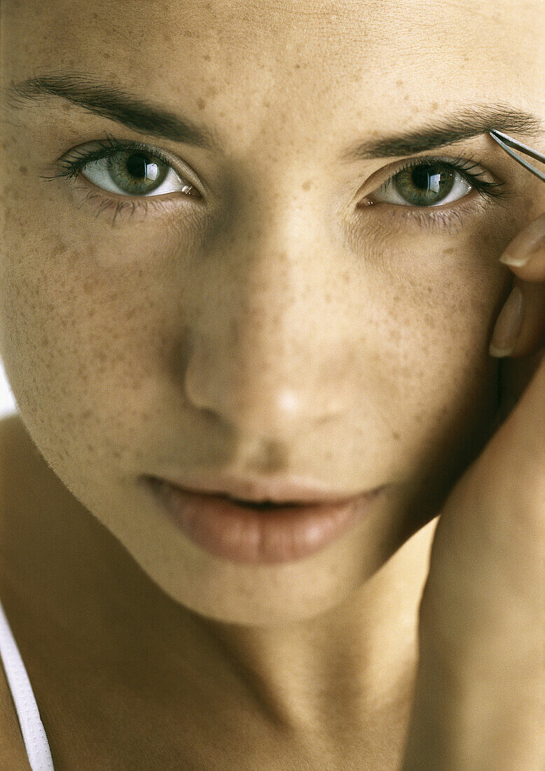 Young woman tweezing eyebrows, close-up