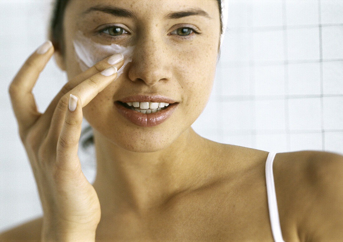 Woman applying moisturizer beneath eye