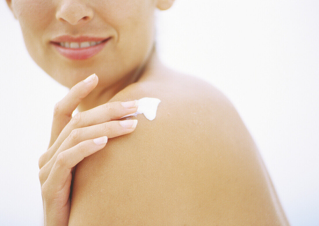 Woman applying sunscreen to shoulder, partial view