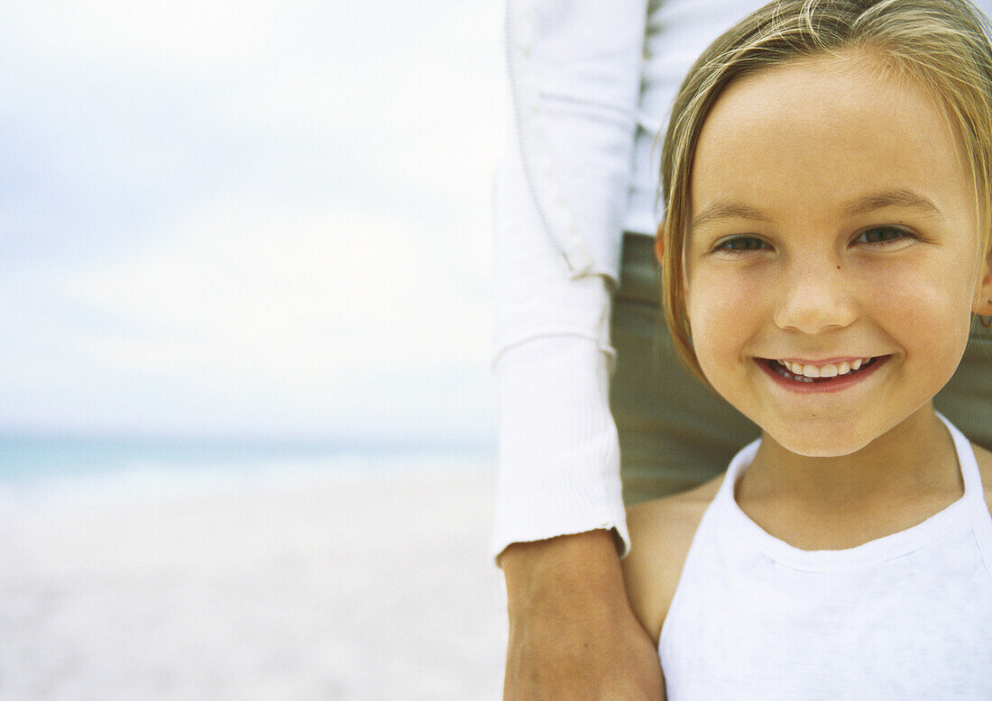 Girl leaning against mother on beach