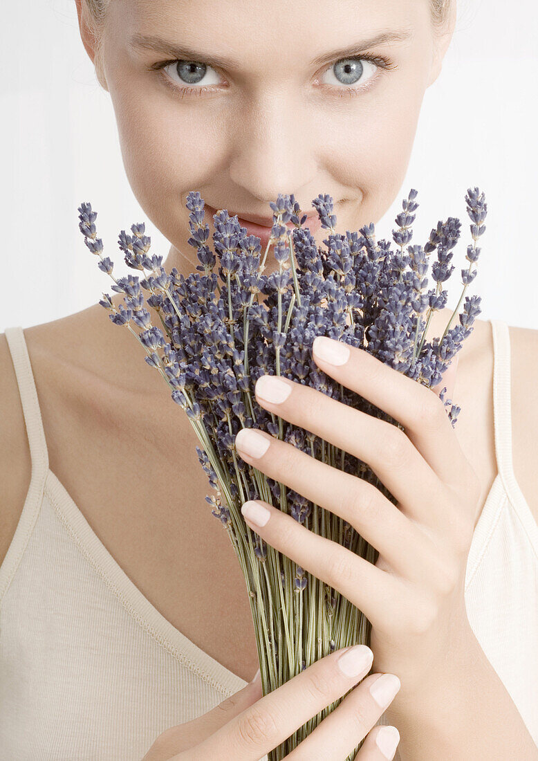 Woman smelling bunch of lavender, looking at camera