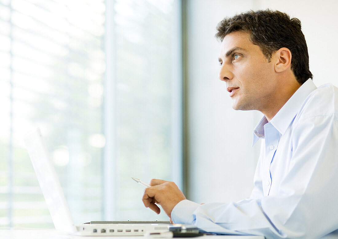 Man sitting at laptop, looking out window