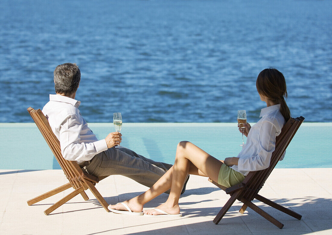 Couple sitting with glasses of champagne, overlooking water