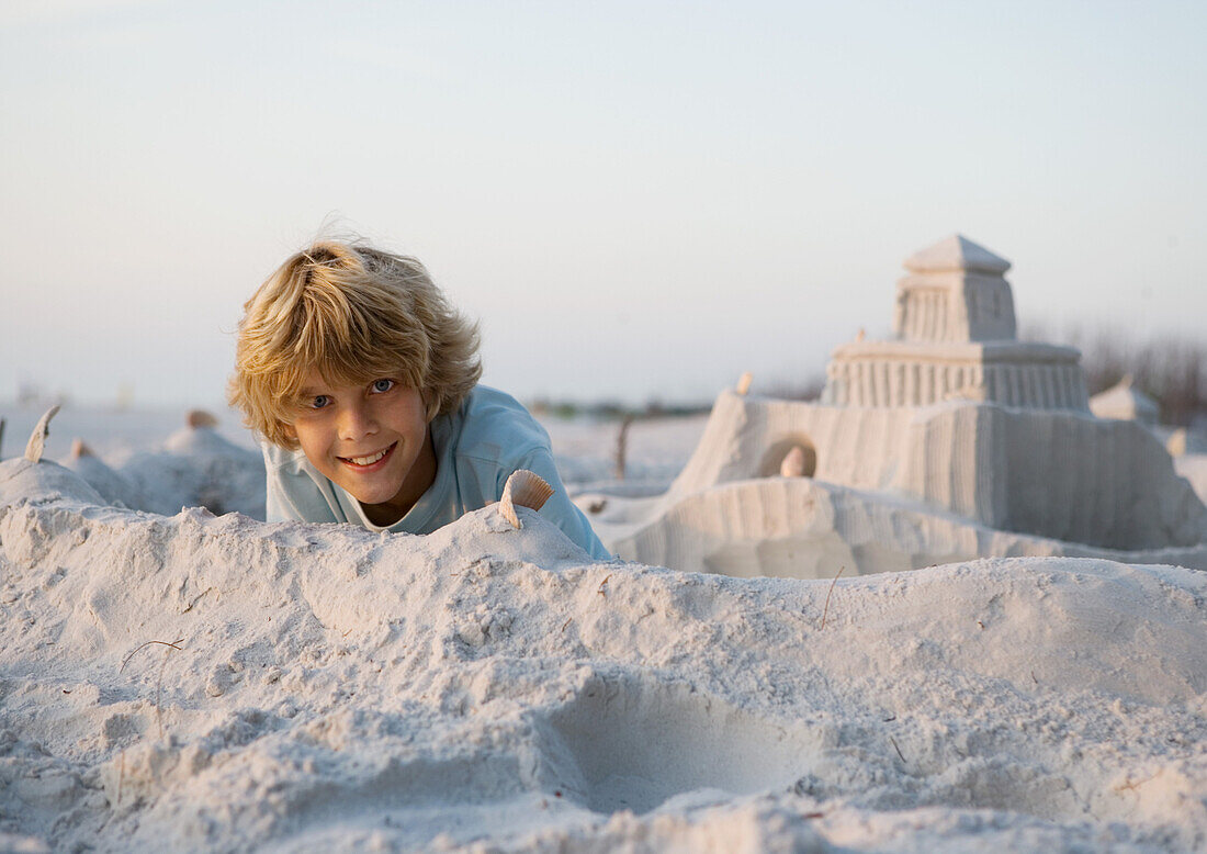 Boy smiling next to sand castle