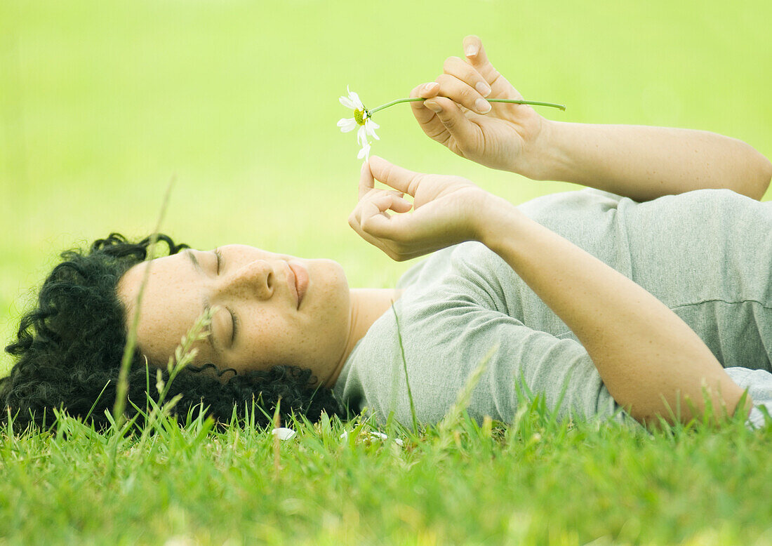Junge Frau im Gras liegend, Blütenblätter von einer Blume pflückend