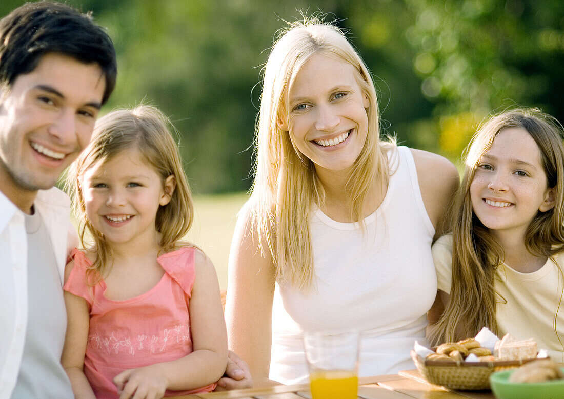 Family sitting at table outdoors, smiling