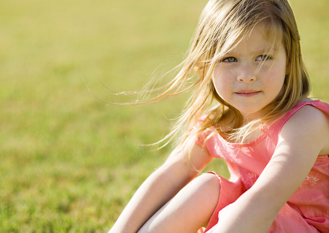 Little girl sitting on grass, hair blowing in wind