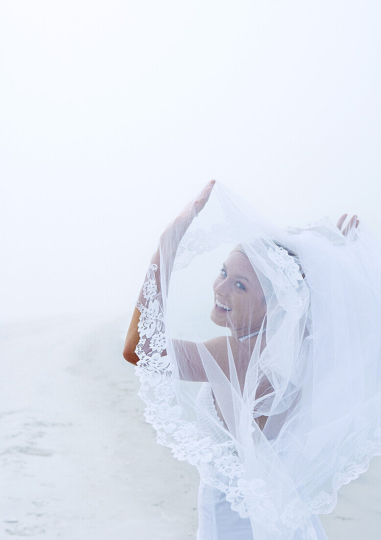 Bride holding up veil on beach