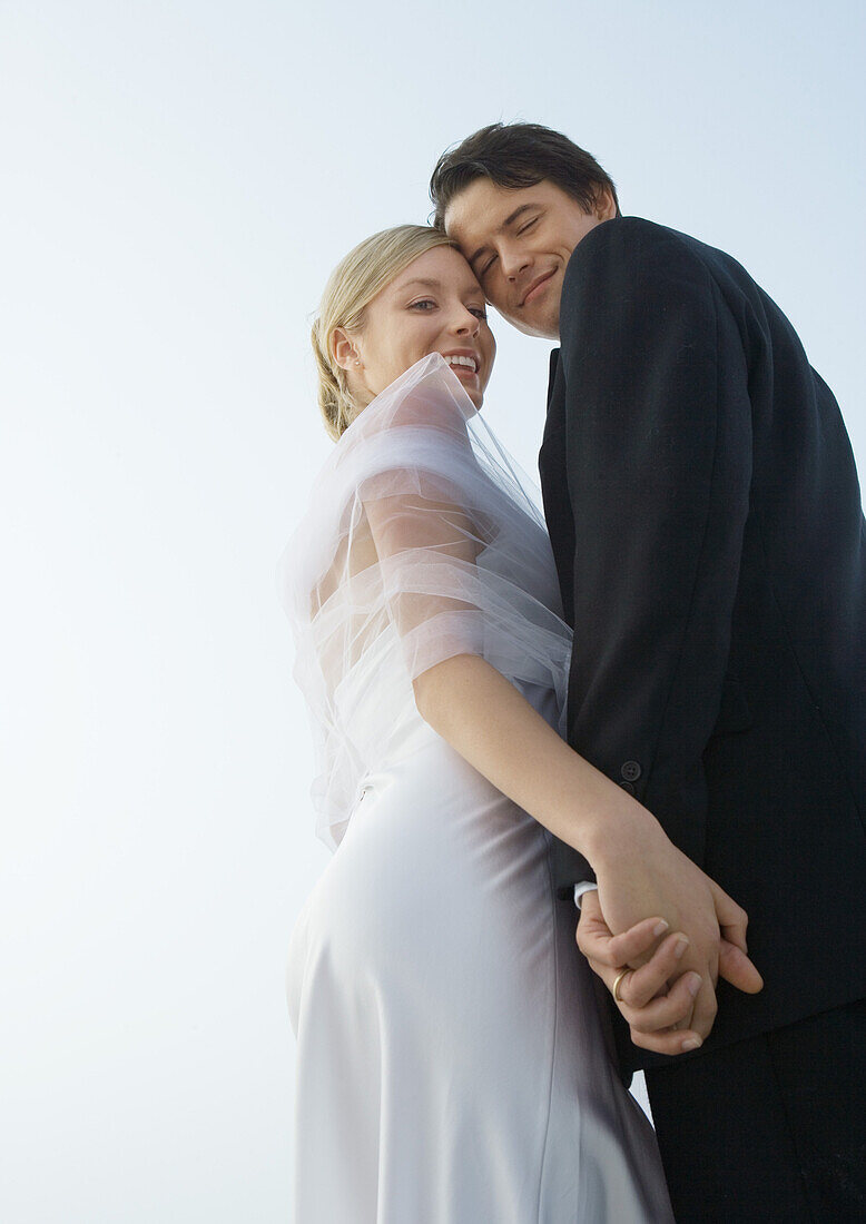 Bride and groom standing close together, holding hands, low angle view