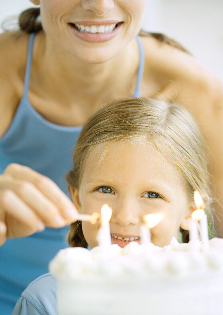 Mother lighting candles on birthday cake for girl