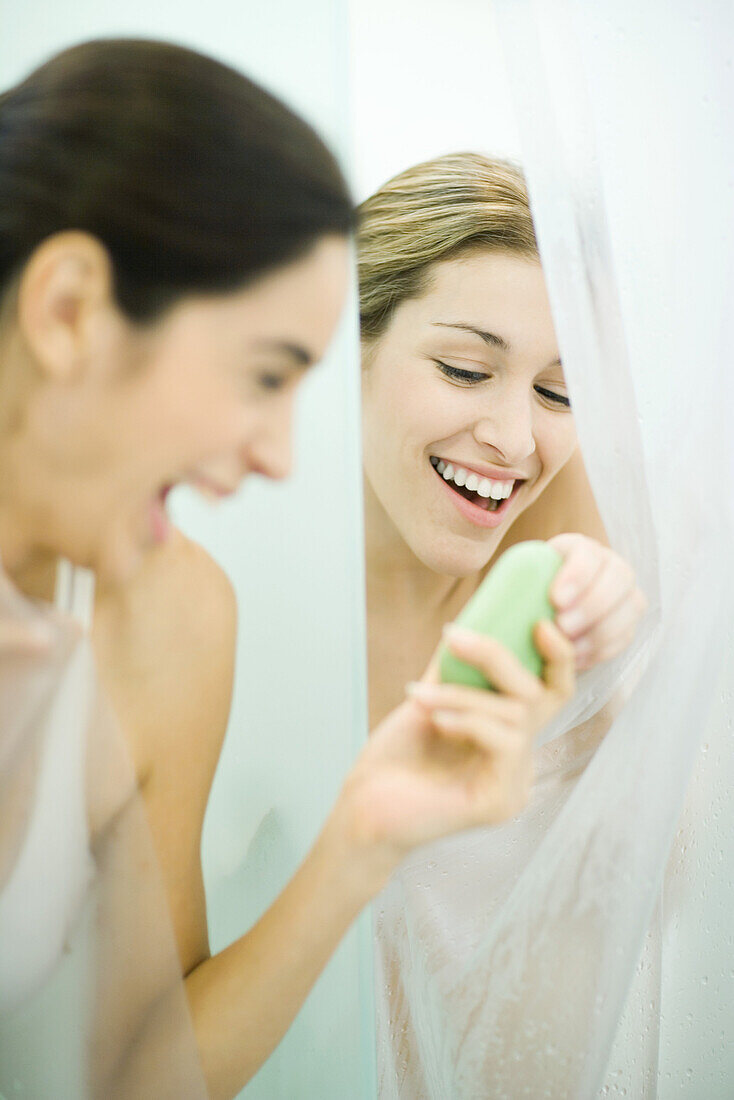 Two young women in showers, one handing bar of soap to the second