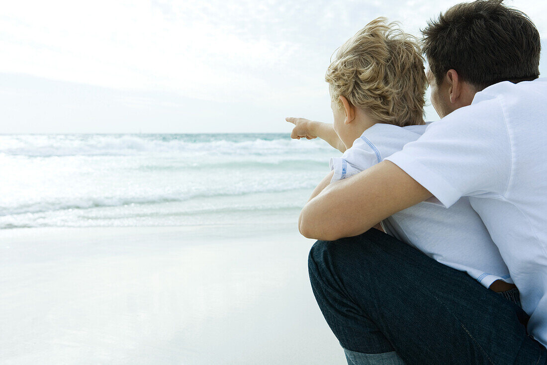 Man looking at ocean with son, rear view