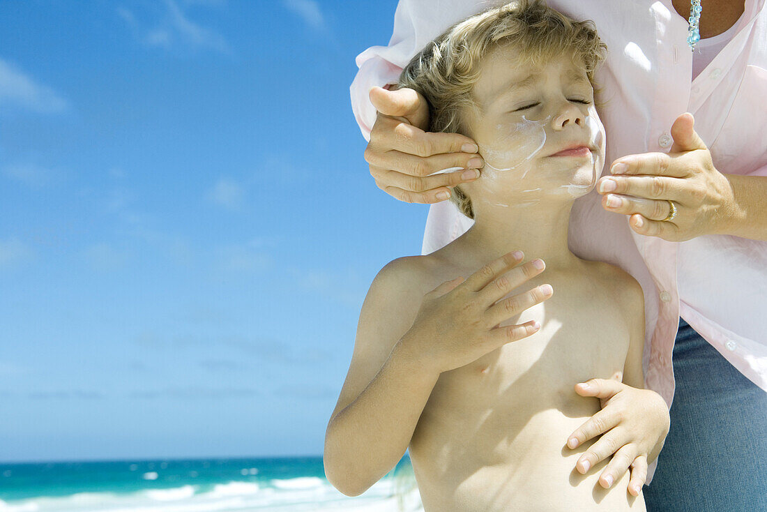 Woman applying sunscreen to son's face on beach