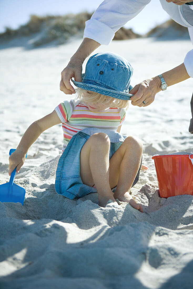 Woman adjusting girl's sunhat on beach