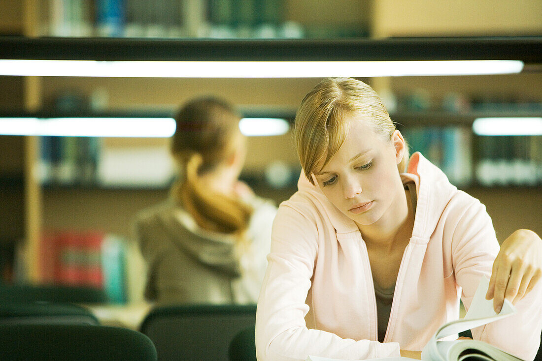 Female college student sitting at table in library, studying