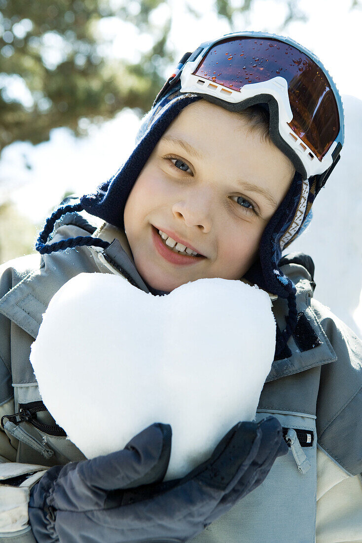 Boy in ski gear holding heart made of snow, portrait