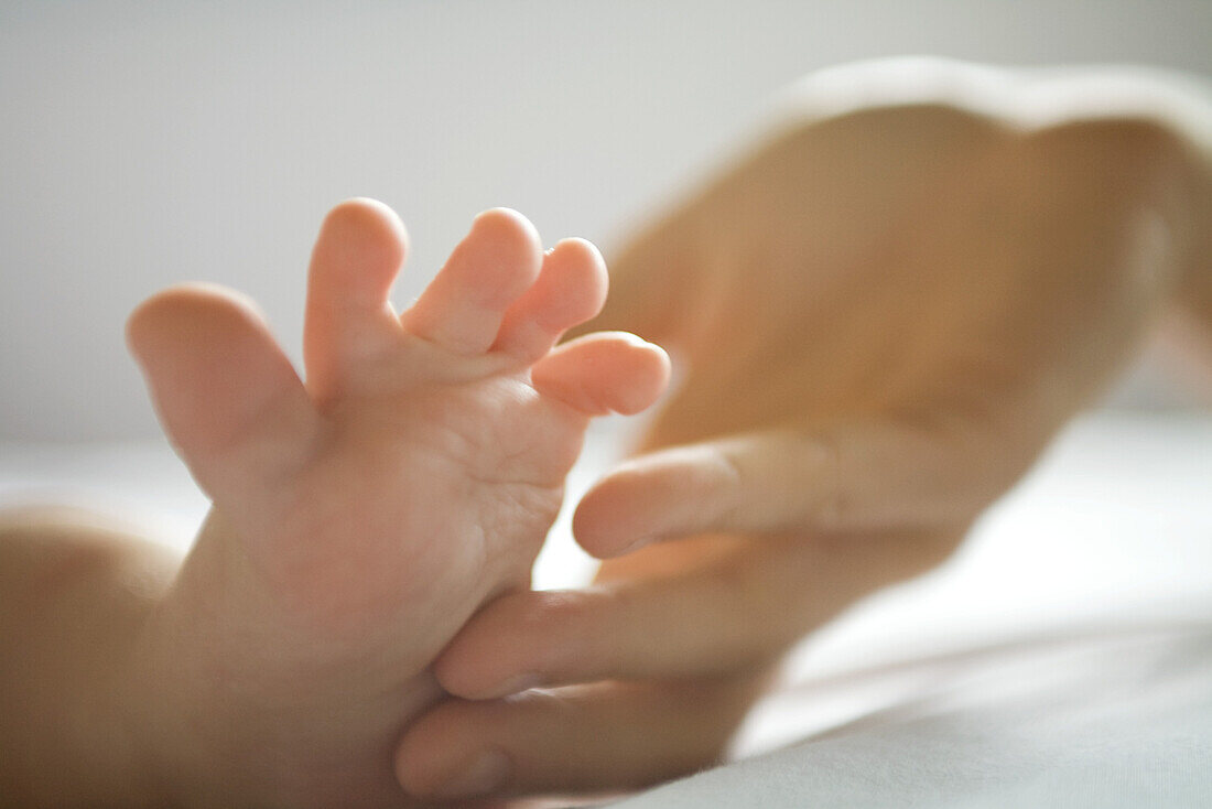 Cropped view of adult hand touching baby's foot, close-up