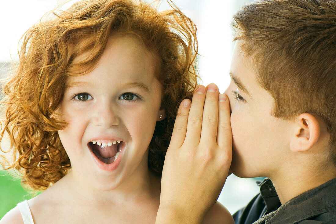 Boy whispering in girl's ear, close-up