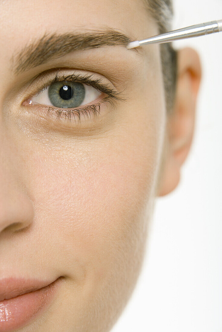 Woman applying make-up to eyebrow, cropped view, close-up