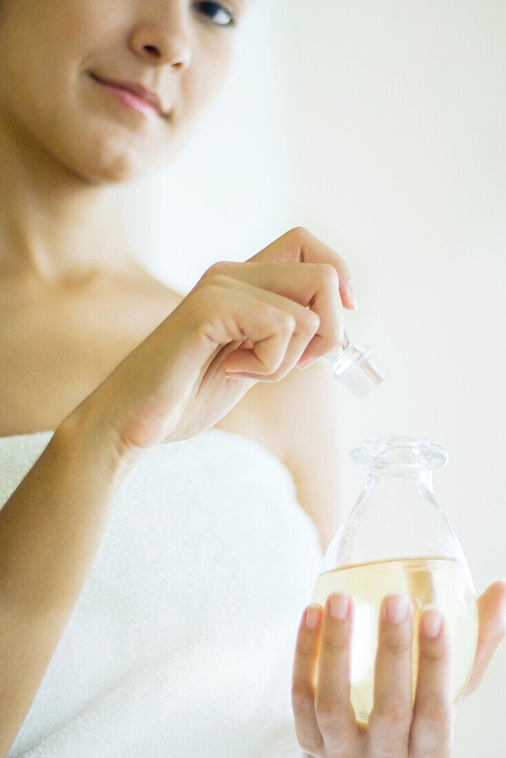 Woman wrapped in towel opening perfume bottle, smiling at camera, cropped view