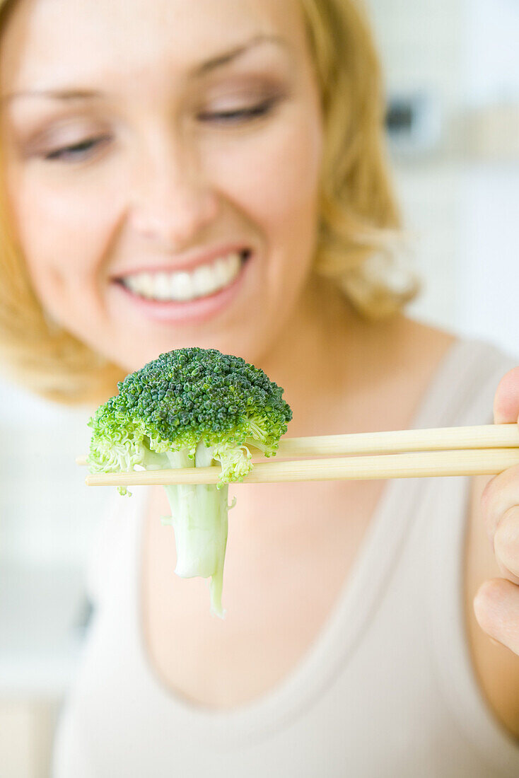 Woman using chopsticks to hold a single piece of broccoli, focus on foreground