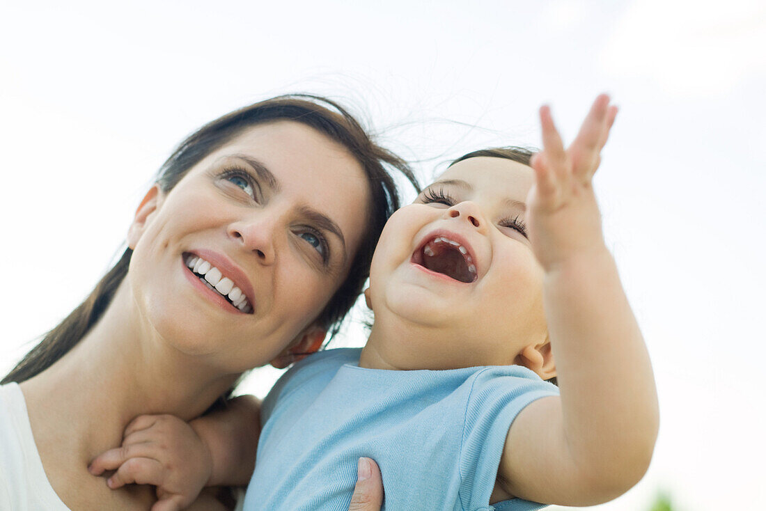 Mother holding baby, both looking up and smiling