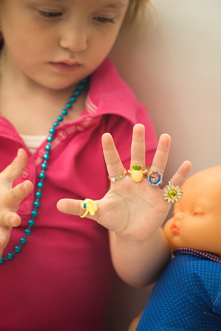 Little girl wearing plastic rings on every finger, looking at hand
