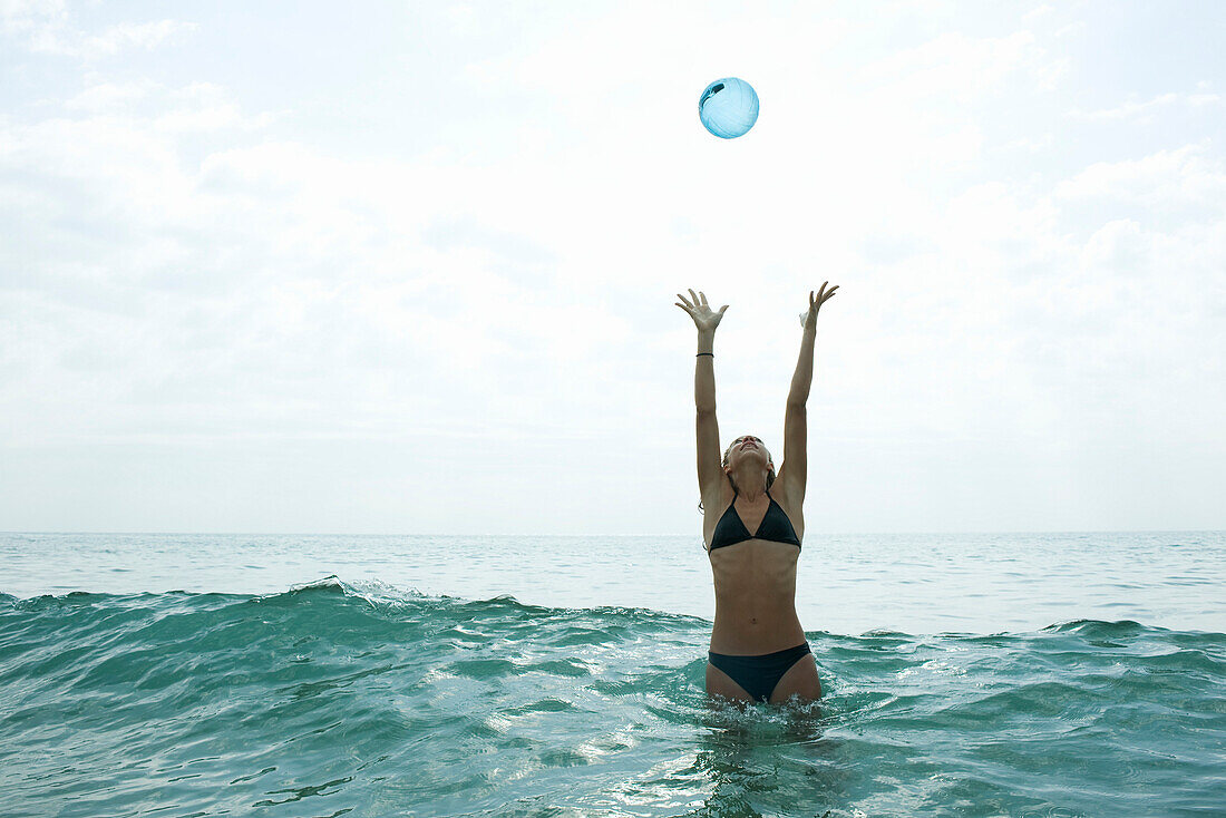 Teen girl in sea with arms raised to catch ball