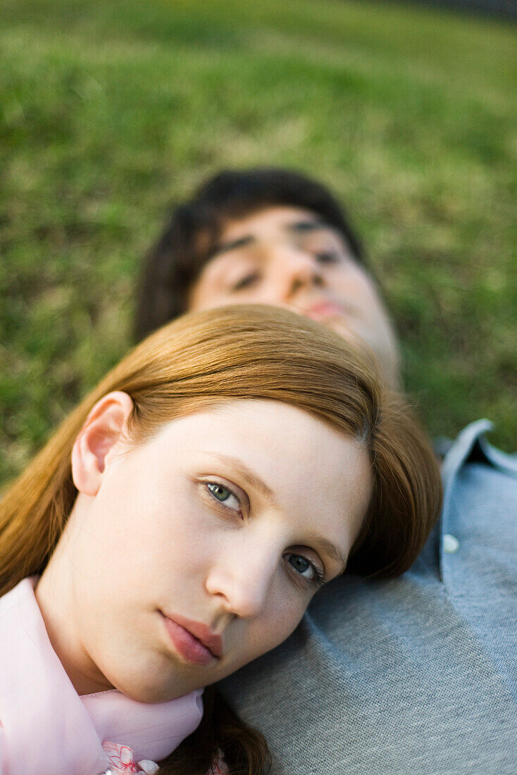 Young couple lying on ground, woman resting head on man's chest, looking at camera