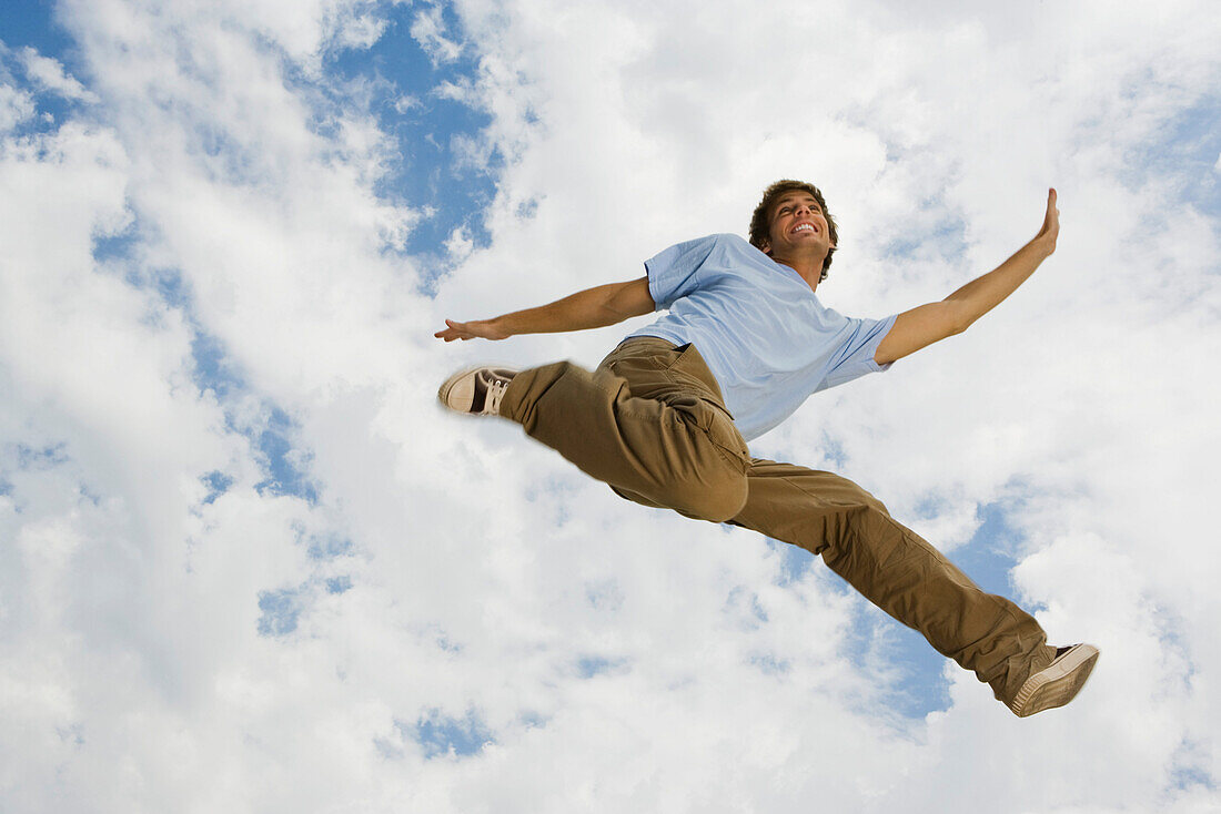 Young man leaping joyfully in midair, low angle view