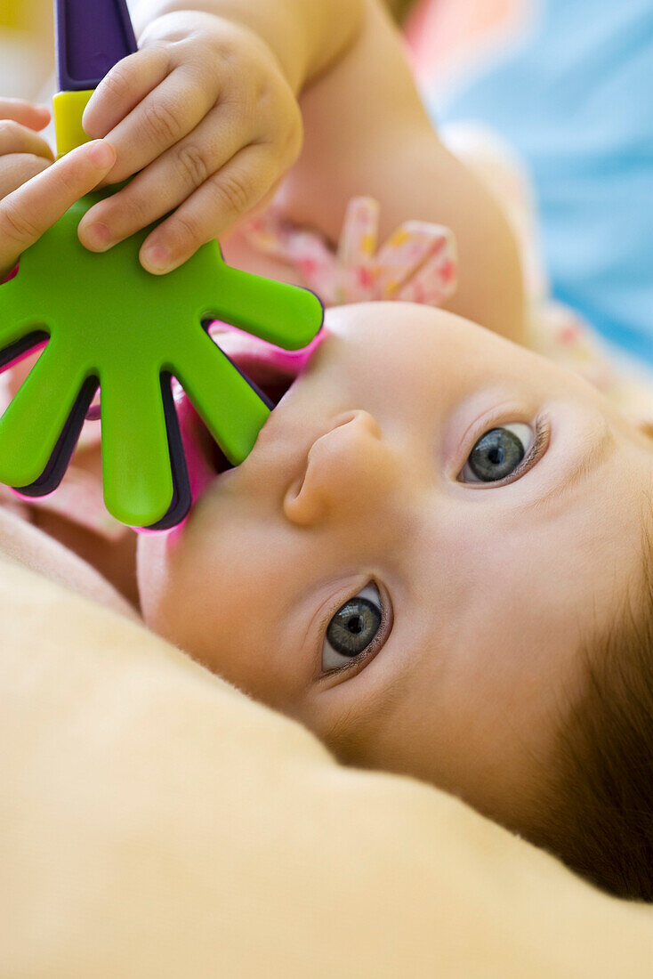 Infant girl chewing on plastic toy, looking at camera