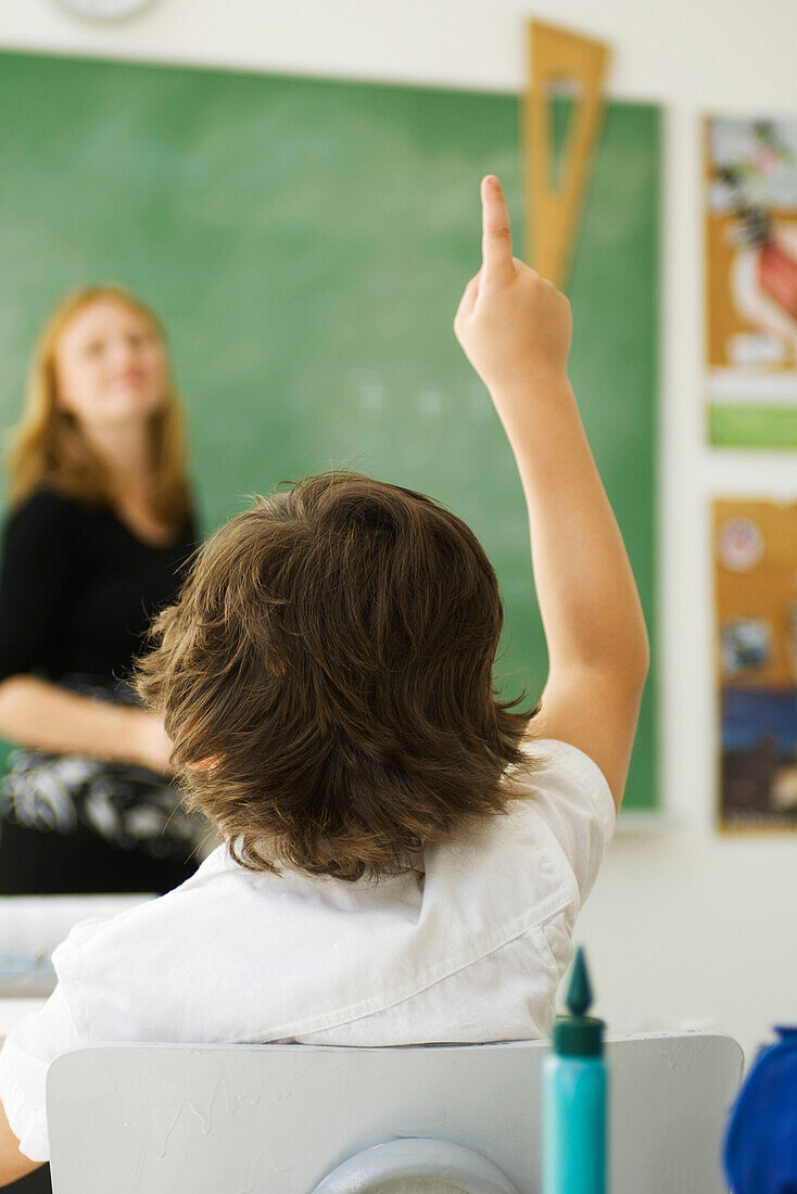 Elementary student raising hand in class, rear view