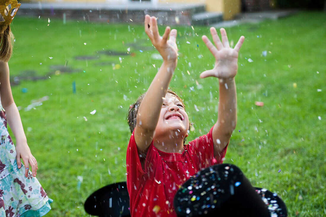 Boy with arms raised showered in falling confetti